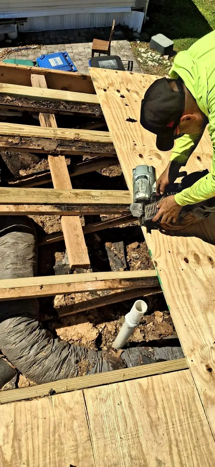 A roofer fastening new plywood over the rafters during a deck repair