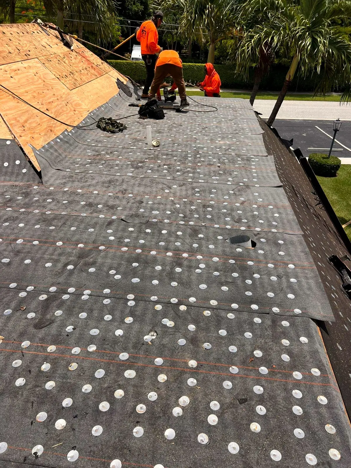 PSR crew members in orange shirts working on a roof deck, with new underlayment fastened in front of them