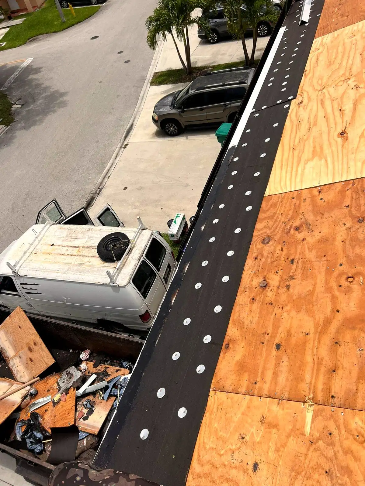 A roof edge dried in over new plywood, with tear-off debris in the truck below